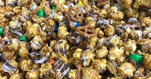 A close-up of a colorful mix of popcorn, pretzels, and candy coated in caramel and chocolate drizzle.