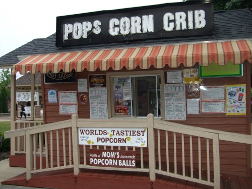 A small popcorn stand with a striped awning, featuring a menu and a sign that reads "World's Tastiest Popcorn."