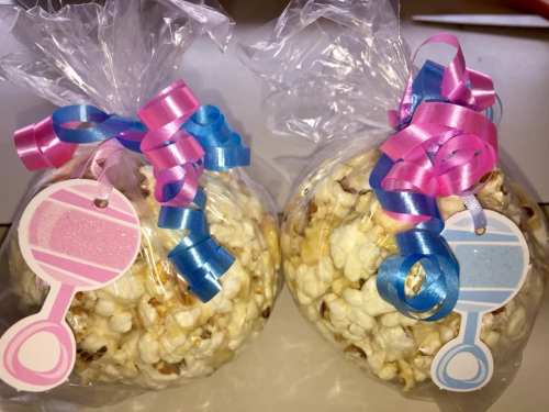 Two bags of popcorn wrapped in clear plastic, decorated with pink and blue ribbons and tags.