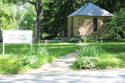 A stone chapel surrounded by greenery and flowers, with a sign reading "Saint Anne's Shell Chapel."