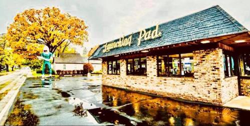 A colorful building named "Launching Pad" with a large green figure outside, surrounded by autumn trees and wet pavement.
