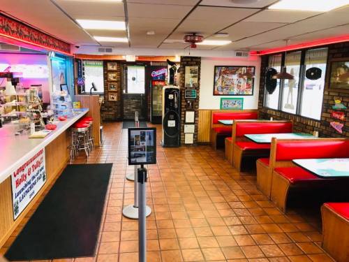 A cozy diner interior with red booths, a counter, and retro decor, featuring a jukebox and colorful lighting.