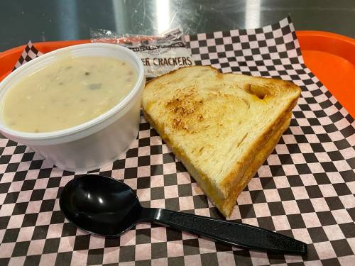 A tray with a bowl of soup, a slice of toasted bread, and a packet of crackers on a checkered paper.