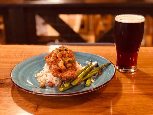 A plate of fried chicken topped with salsa, served with rice and asparagus, alongside a glass of dark beer.