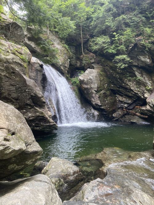 A serene waterfall cascades into a clear pool, surrounded by rocky cliffs and lush greenery.