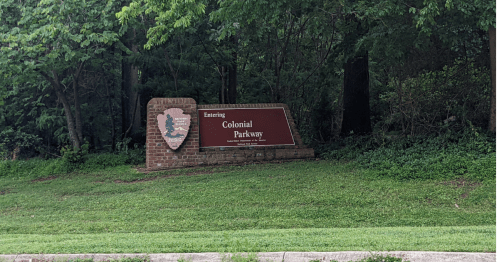 Sign marking the entrance to Colonial Parkway, surrounded by greenery and trees.