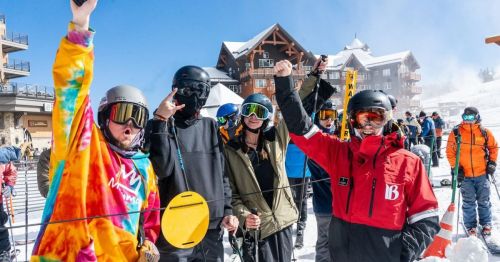 A group of excited skiers in colorful gear celebrate on a snowy mountain slope.