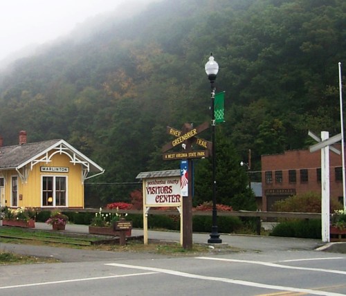 A foggy scene featuring a visitors center sign, trail markers, and a quaint yellow building in a mountainous area.