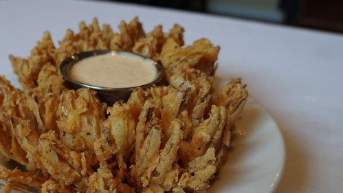 A large, golden-brown onion blossom served with a small bowl of dipping sauce in the center.
