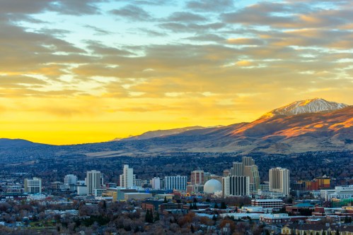 A panoramic view of a city skyline at sunset, with mountains in the background and a mix of buildings in the foreground.