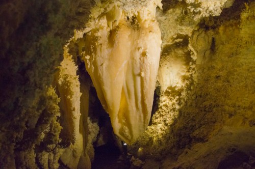 A dimly lit cave interior featuring large, stalactite formations hanging from the ceiling.
