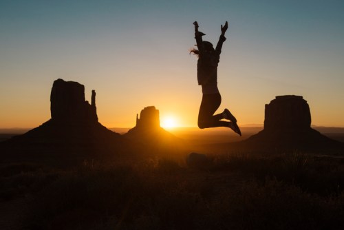 A person jumps joyfully against a sunset backdrop with iconic rock formations in the foreground.