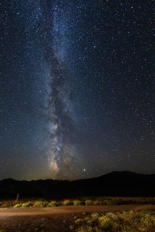 A stunning night sky filled with stars and the Milky Way, above a dark landscape and distant mountains.
