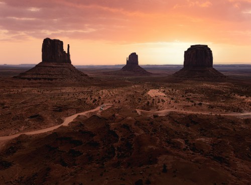 A stunning sunset over Monument Valley, featuring iconic rock formations and a winding dirt road in the foreground.