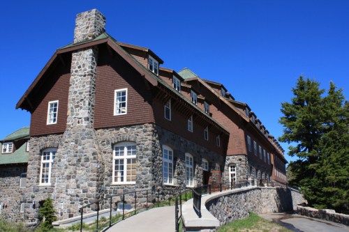 Historic stone building with a sloped roof, surrounded by greenery and a clear blue sky.