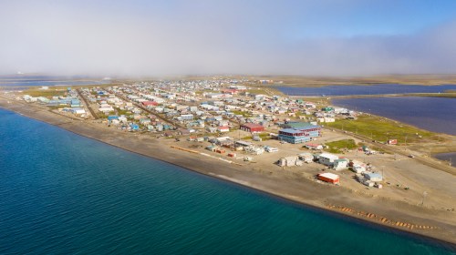 Aerial view of a coastal town with colorful buildings, surrounded by water and foggy landscape.