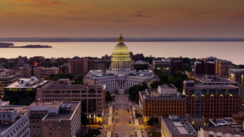 Aerial view of a city at sunset, featuring a prominent dome building and a lake in the background.