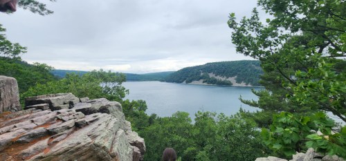 A scenic view of a lake surrounded by lush greenery and rocky cliffs under a cloudy sky.