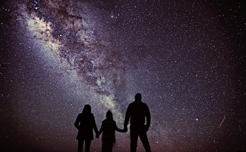 Silhouetted figures of a family holding hands under a starry night sky with the Milky Way visible.