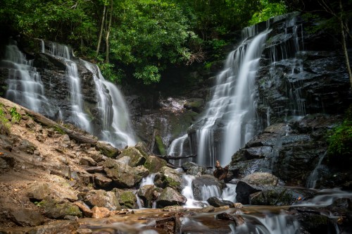 A serene waterfall cascades over rocky terrain, surrounded by lush green foliage in a tranquil forest setting.