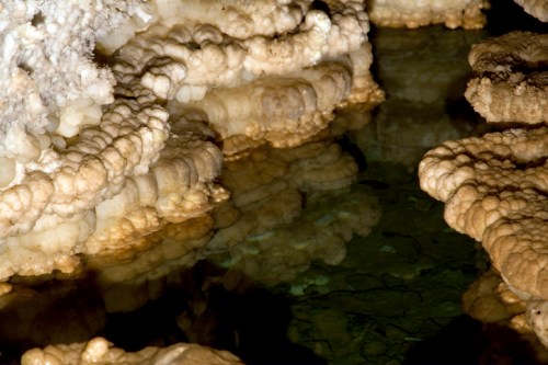 Stalactite formations and reflections in a dark, still underground pool.