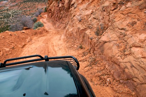 A close-up view from a vehicle's roof, showing a rugged, winding dirt road along rocky terrain.