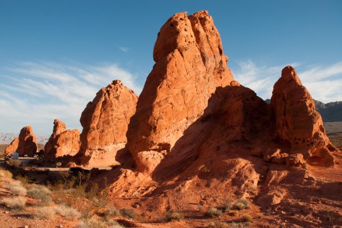 A landscape featuring towering red rock formations under a clear blue sky, with sparse vegetation in the foreground.