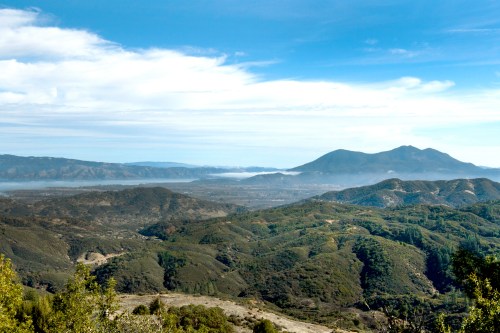 A panoramic view of rolling green hills and mountains under a blue sky with scattered clouds.