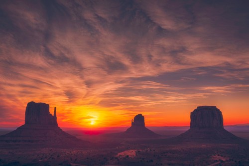 Sunset over Monument Valley, featuring iconic rock formations silhouetted against a colorful sky.
