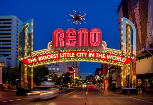 Neon sign reading "Reno: The Biggest Little City in the World" illuminated at night, with city buildings in the background.