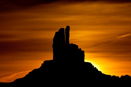 Silhouette of a rock formation against a vibrant orange and yellow sunset sky.