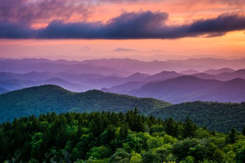 A stunning sunset over layered mountains, with vibrant colors and lush green forests in the foreground.