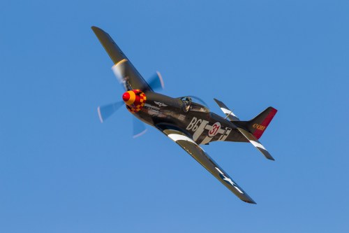 A vintage fighter plane flying against a clear blue sky, showcasing its colorful propeller and sleek design.