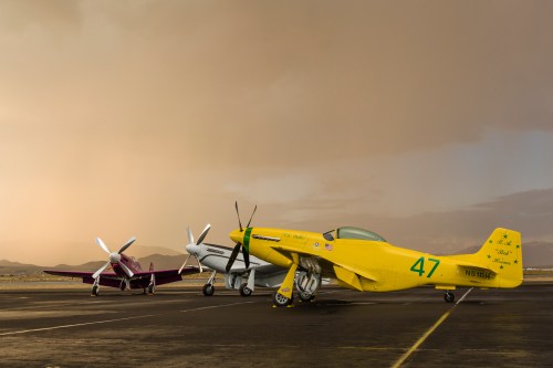Three vintage aircraft parked on a runway under a dramatic sky, showcasing their colorful designs.
