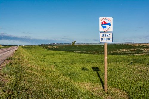 A sign for the Nebraska Byways, indicating "Bridges to Buttes," beside a wide, green field and a clear blue sky.