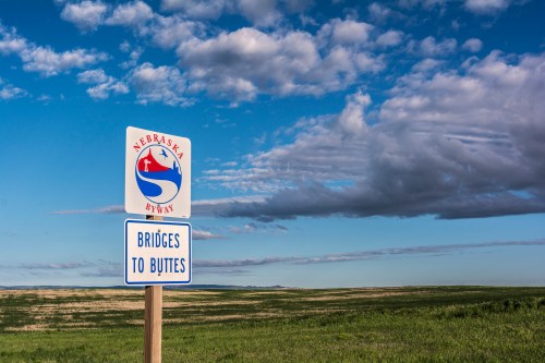 Sign for Nebraska Byway with "Bridges to Buttes" against a backdrop of blue sky and green fields.