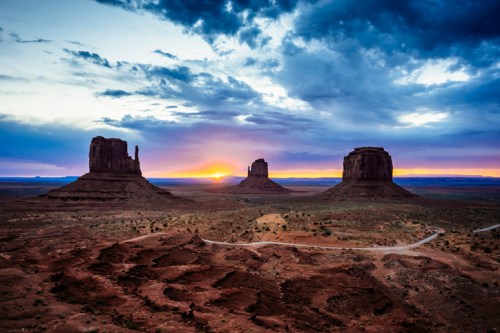 Sunset over Monument Valley, featuring iconic rock formations and a dramatic sky with clouds.