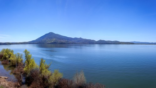 A serene lake surrounded by lush greenery and mountains under a clear blue sky.