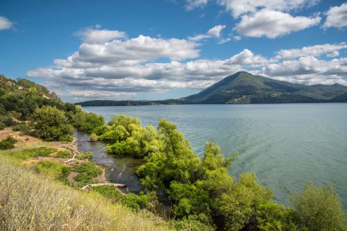 A serene lake surrounded by lush greenery and mountains under a partly cloudy sky.