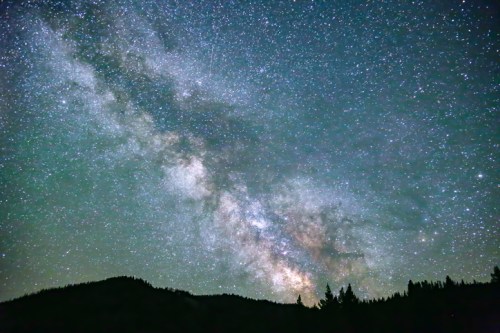 A stunning view of the Milky Way galaxy filled with stars, set against a dark silhouette of mountains.