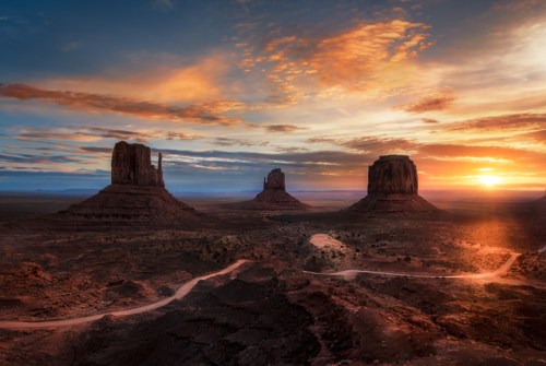 A stunning sunset over Monument Valley, highlighting towering rock formations and a winding dirt road.