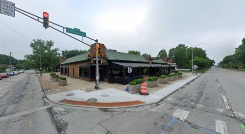 A corner restaurant with a green roof, surrounded by planters, at a traffic light intersection on a cloudy day.