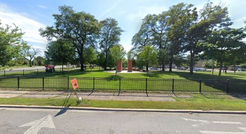 A park with green grass and trees, featuring a monument and a construction sign in the foreground.