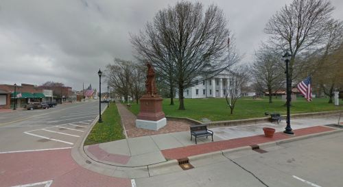 A town square featuring a statue, trees, and a historic building, with American flags and benches lining the street.
