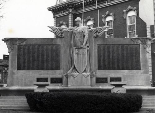 A historic monument featuring a statue and engraved plaques, set against a building backdrop.