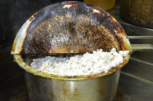 A pot of freshly popped popcorn with a slightly burnt lid, showing remnants of oil and seasoning.
