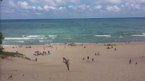 A sandy beach with people enjoying the sun, gentle waves, and a cloudy sky in the background.