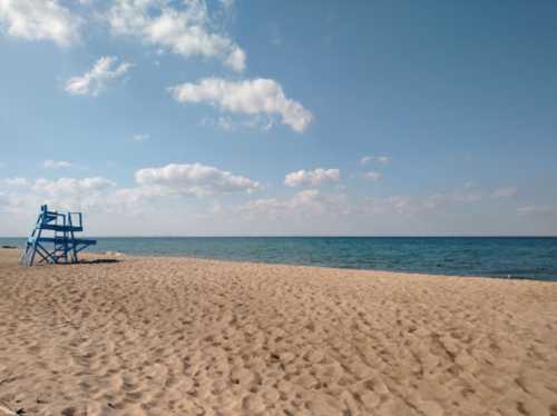 A sandy beach with a blue lifeguard tower and calm ocean under a partly cloudy sky.