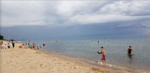 A beach scene with people swimming and playing in the water under a cloudy sky. Sand and shoreline are visible.