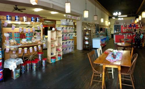 A cozy shop interior with colorful displays, wooden tables, and shelves filled with various products and treats.